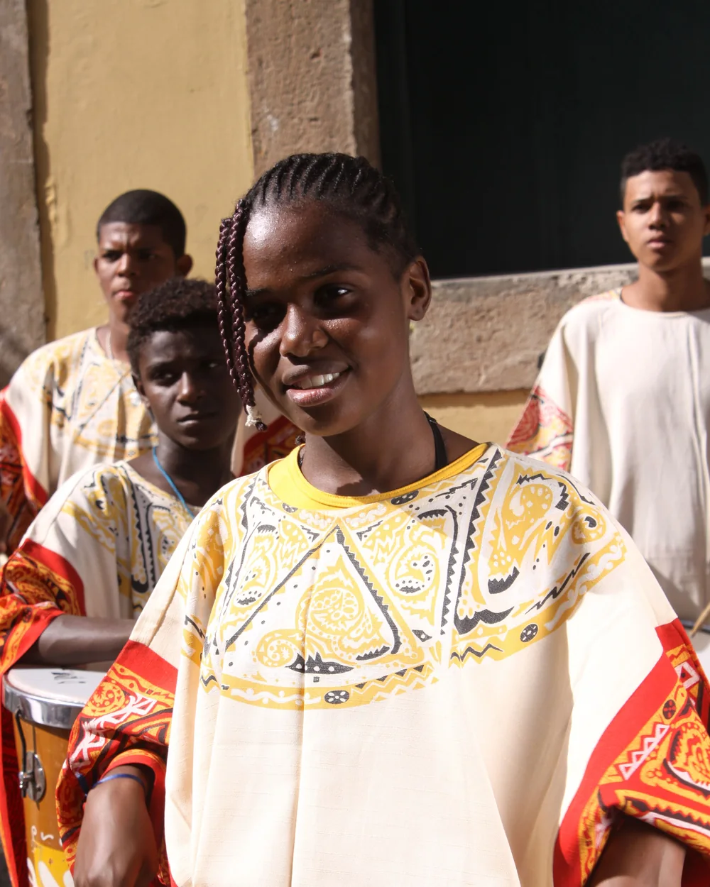 A young Bahian drummer in a yellow and white costume plays a hand drum, Salvador